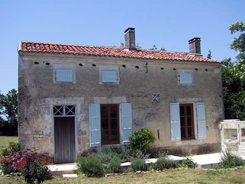 Façade of house: shrubs in bloom in early summer, rebuilt BBQ on the right